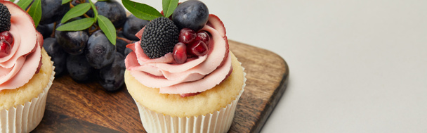 panoramic shot of cupcakes with cream and berries on cutting board isolated on grey - Photo, Image