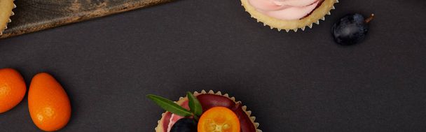 panoramic shot of cupcakes with kumquats on black surface - Foto, afbeelding