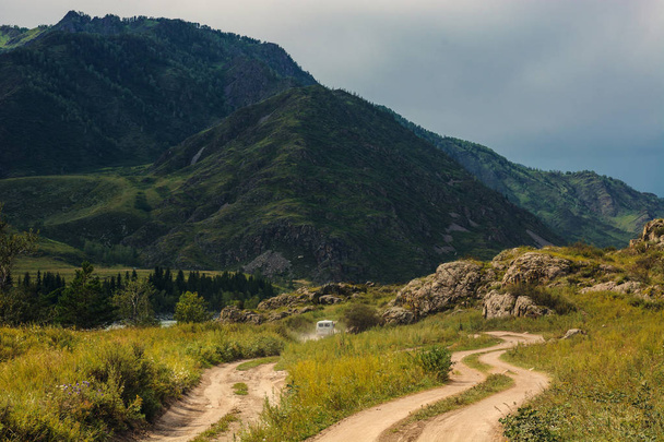 The car is moving forward along a dirt road among the mountains and hills. Mountain Altai. - Photo, Image