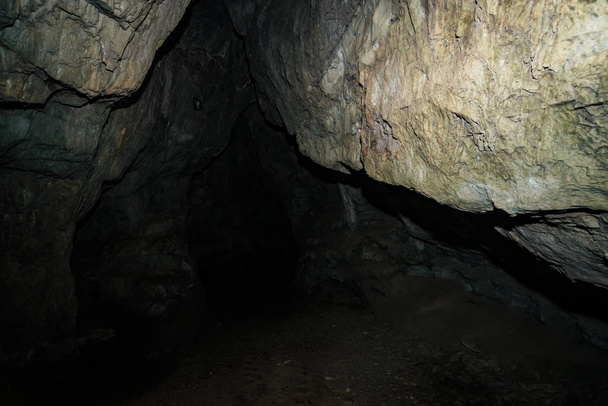 美しい洞窟だ暗いダンジョンの中からの眺め。洞窟のテクスチャードの壁。地下トンネルの背景画像。洞窟内の湿気。トンネルの終点の光. - 写真・画像