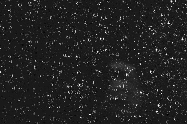 Dirty window glass with drops of rain. Atmospheric monochrome dark background with raindrops. Droplets and stains close up. Detailed transparent texture in macro with copy space. Night rainy weather. - Photo, Image