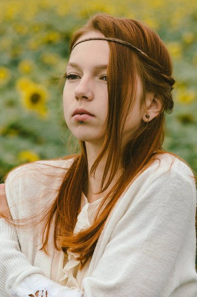 Retrato delicado de uma menina de cabelos vermelhos vestida em um estilo vintage contra o fundo de um campo com girassóis. Processamento artístico. Maquilagem natural
. - Foto, Imagem