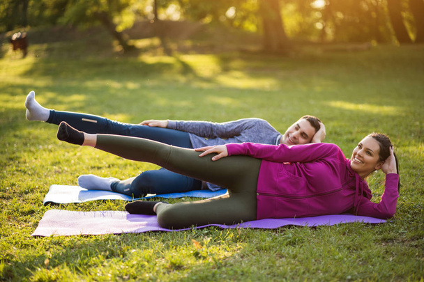 Couple is exercising in park. Exercise for sciatica recovery. - Valokuva, kuva