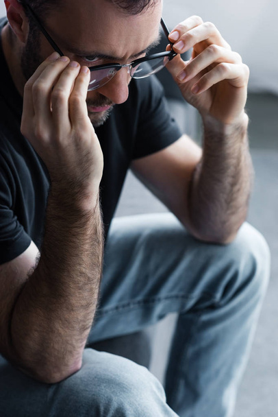 αναστατωμένος άνθρωπος αγγίζοντας γυαλιά ενώ κάθεται στον καναπέ στο σπίτι - Φωτογραφία, εικόνα