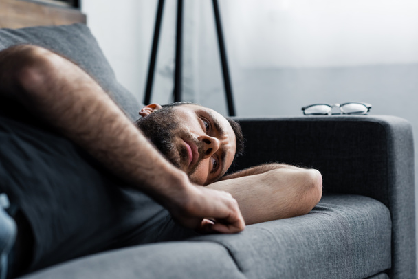 depressed man lying on grey sofa at home and looking away - Photo, image