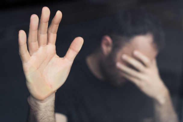 selective focus of depressed man standing by window with hand on face - Фото, изображение