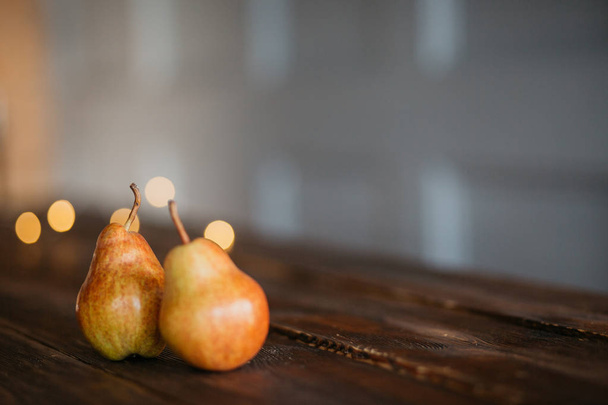 Beautiful ripe tasty pears on a large kitchen wooden table with a garland of lights. A beautiful screen saver for an article about wholesome food, a concept for a food blog, a saver for a pastry chef - Photo, image