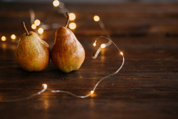 Beautiful ripe tasty pears on a large kitchen wooden table with a garland of lights. A beautiful screen saver for an article about wholesome food, a concept for a food blog, a saver for a pastry chef - Photo, Image