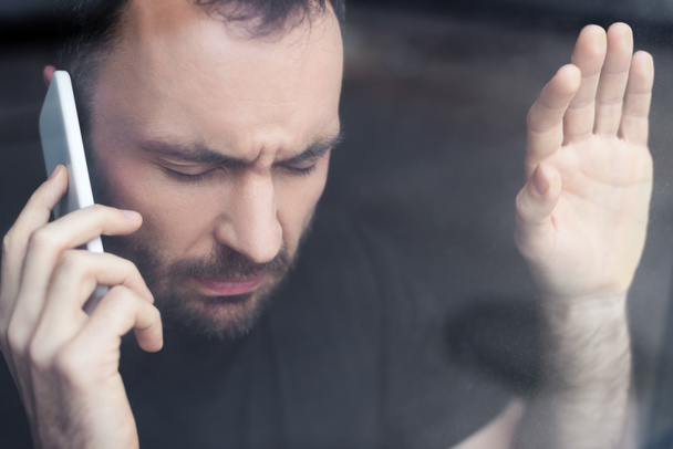стресова людина з закритими очима тримає смартфон, стоячи біля вікна
 - Фото, зображення