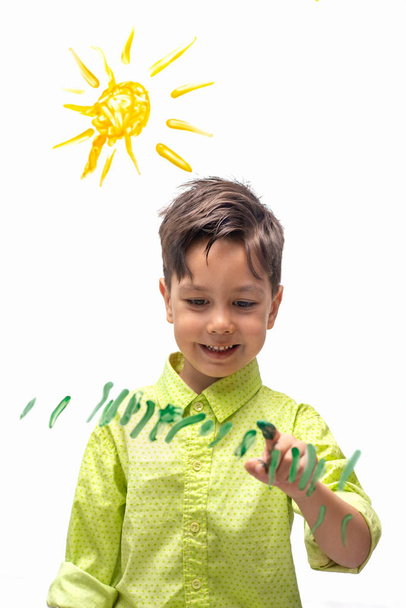 Το μικρό αγόρι που φοράει πράσινο πουκάμισο ζωγραφίζει με ενθουσιασμό τον ήλιο - Φωτογραφία, εικόνα