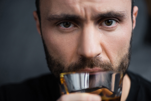 selective focus of depressed man holding glass of whiskey and looking at camera - Foto, Imagen
