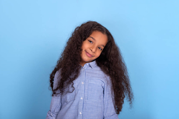 Waist up  portrait of smiling mulatta frizzy girl wearing blue shirt on a blue background with copy space. - Foto, Imagem