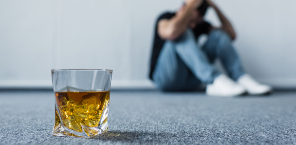 foyer sélectif de l'homme déprimé assis sur le sol par mur près du verre de whisky
 - Photo, image