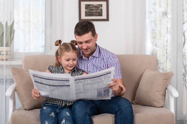 Little daughter and dad sitting on the sofa at home and reading  - Фото, изображение
