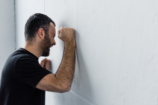 дорослий депресивний чоловік кричить, стоячи біля білої стіни вдома
 - Фото, зображення