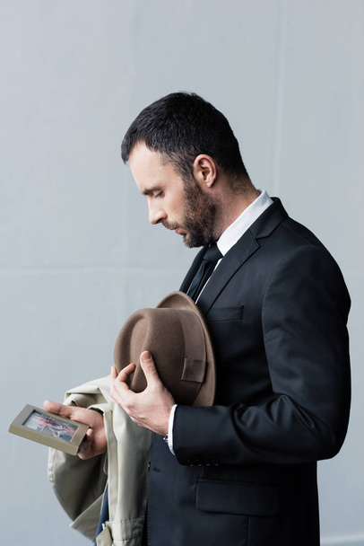 hombre deprimido en traje mirando la foto en el marco mientras sostiene el sombrero en la mano
 - Foto, imagen