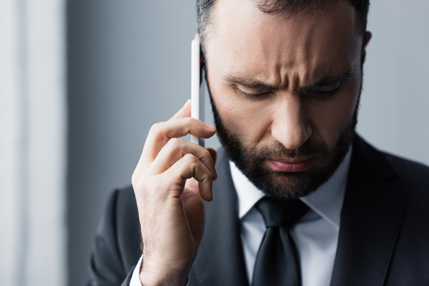 serious bearded man in black suit looking down while using smartphone - Foto, imagen