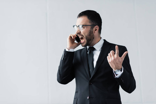 angry businessman in black suit and glasses quarreling while talking on smartphone - Foto, immagini