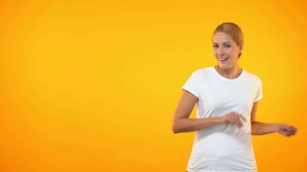 Attractive female pointing fingers on orange background, template presentation - Felvétel, videó