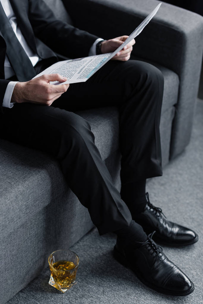 businessman sitting on sofa with newspaper near glass of whiskey on floor - Φωτογραφία, εικόνα