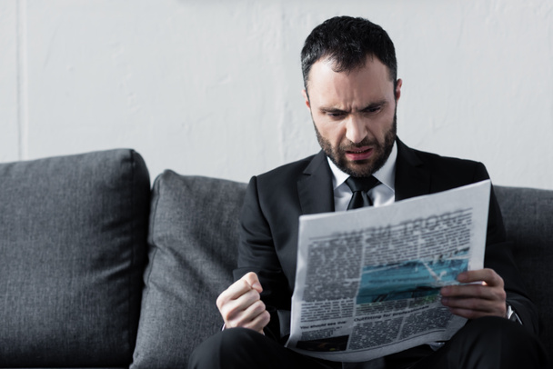 bearded worried businessman reading newspaper while sitting on sofa - 写真・画像
