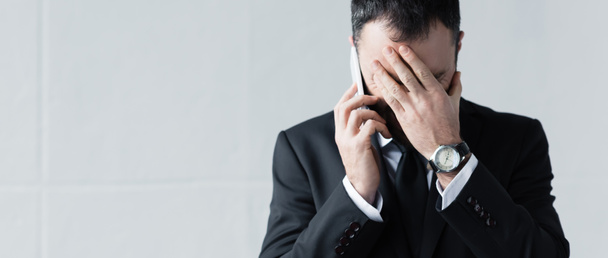 панорамний знімок засмученого бізнесмена, який тримає руку на обличчі під час використання смартфона
 - Фото, зображення