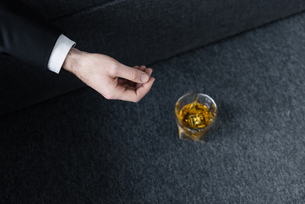 partial view of man lying on sofa near glass of whiskey on floor - Fotografie, Obrázek