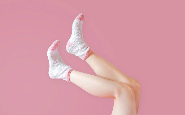 ピンクの背景にファッションソックスを持つ女性の足。冬の靴下を履く. - 写真・画像
