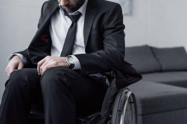 cropped view of disabled man in black suit sitting in wheelchair with bowed head - 写真・画像
