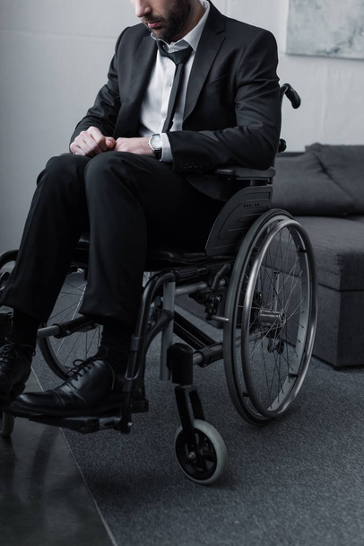обрізаний вид на бородатого чоловіка з обмеженими можливостями в чорному костюмі, що сидить у інвалідному візку
 - Фото, зображення