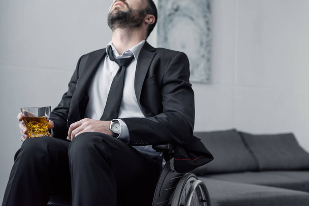 vista recortada del hombre discapacitado deprimido en traje sentado en silla de ruedas con vaso de whisky
 - Foto, Imagen