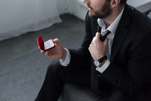 high angle view of sitting man in suite holding red gift box with ring - Foto, afbeelding