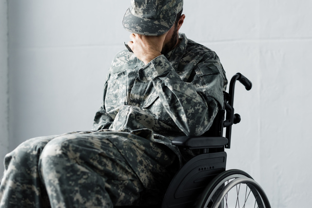 depressed disabled military man in uniform sitting in wheelchair and covering face with hand - Foto, Bild