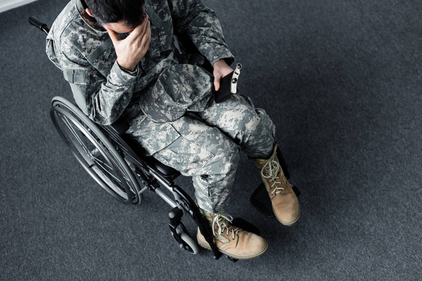 overhead view of disabled military man in uniform sitting with flask in wheelchair and covering face with hand - Φωτογραφία, εικόνα