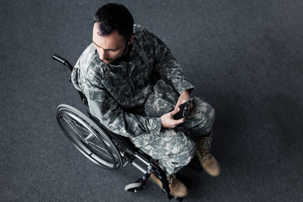 tekerlekli sandalyede oturan ve elinde şapka tutan üniformalı engelli adamın havai görünümü - Fotoğraf, Görsel