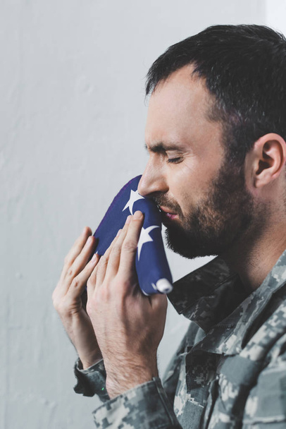 depressed bearded military man crying while kissing usa national flag - 写真・画像