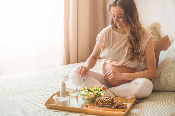 Gravidez e nutrição orgânica saudável. Mulher grávida desfrutando de salada de legumes frescos na cama, espaço livre
 - Foto, Imagem