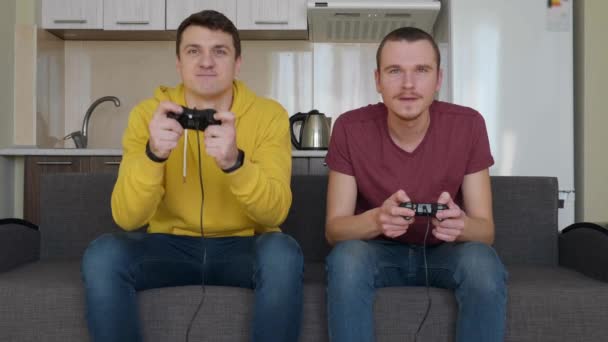 Two men are playing video game and win. Young guys are sitting on the couch, hold gamepads in their hands, play console, enjoy the victory and give five to each other. Team match. 4K footage. - Footage, Video