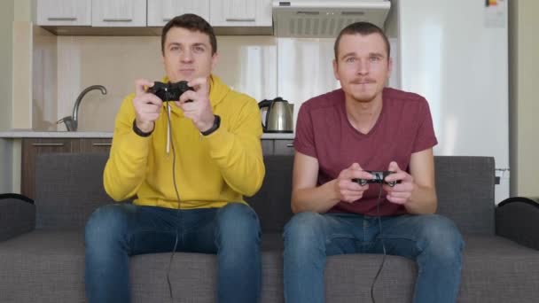 Двое мужчин играют в видеоигры и выигрывают. Молодые парни сидят на диване, держат в руках геймпады, играют на консоли, наслаждаются победой и дают друг другу пять. Командный матч. 4K видео
. - Кадры, видео