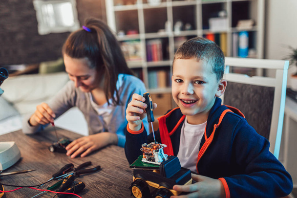 Щасливий усміхнений хлопчик і дівчинка конструюють технічну іграшку і роблять грабунок
 - Фото, зображення