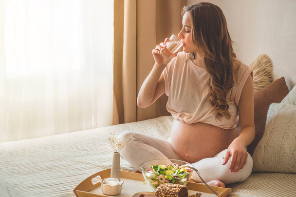 Pregnancy and healthy organic nutrition. Pregnant woman enjoying fresh vegetable salad in bed, free space - Foto, afbeelding