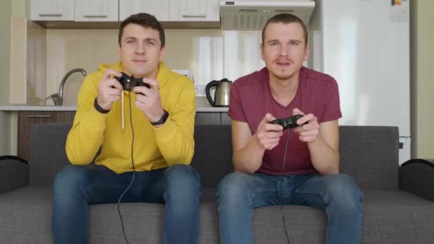 İki adam video oyunu oynuyor ve kaybediyor. Genç çocuklar kanepede oturuyor, ellerinde gamepads tutun ve konsol oynamak, düzeyleri nin geçişi sırasında hatalarını tartışmak. Takım maçı. 4k görüntü. - Video, Çekim