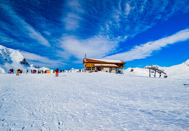 hiihtokeskus kaukaisten ihmisten kanssa, rakennus ja köysirata sinisen taivaan alla
 - Valokuva, kuva