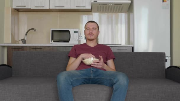Un uomo sta guardando la TV. Un ragazzo noioso seduto sul divano, che mangia popcorn e guarda uno show televisivo. Una cucina sullo sfondo. Filmati 4K
. - Filmati, video