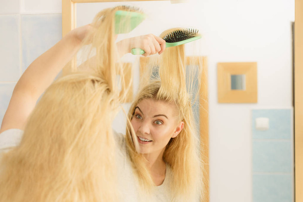 Woman brushing her blonde hair in bathroom - Foto, afbeelding