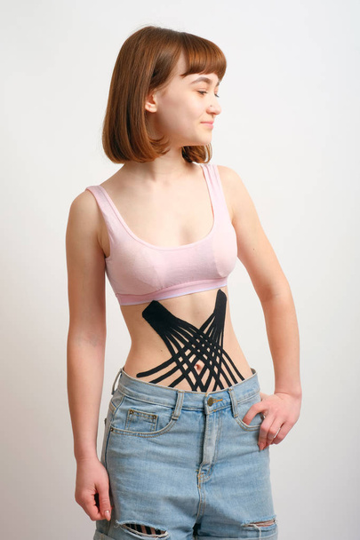 Crossed kinesio tape on the abdomen of young girl on white background. - Fotografie, Obrázek