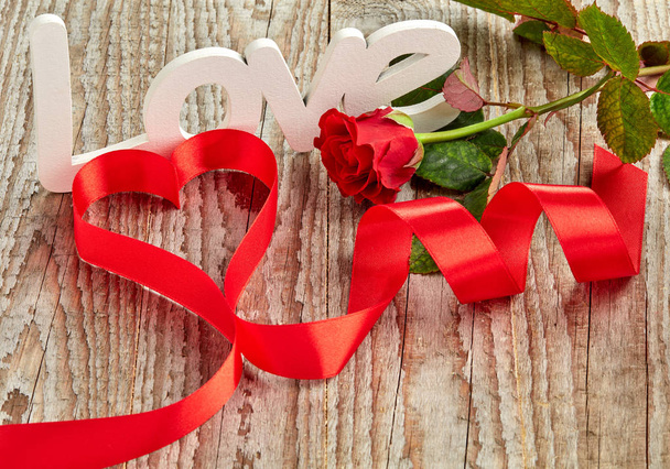 白い愛の看板とバラと木製の背景に赤いカールリボン - 写真・画像