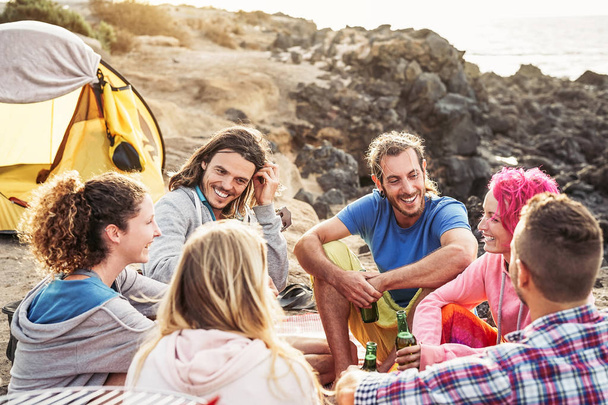 Grupo de amigos felices acampando junto a la playa al atardecer - Jóvenes divirtiéndose y bebiendo cerveza al aire libre - Millennial, verano, vacaciones y vacaciones juveniles concepto de estilo de vida
 - Foto, imagen