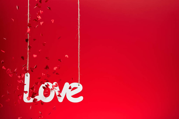 Wit liefdesbord met vallende confetti op rode achtergrond - Foto, afbeelding