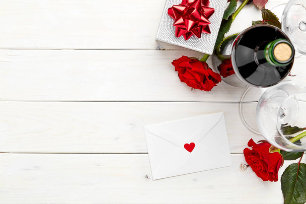 Σύνθεση του μπουκάλι κόκκινο κρασί στο λευκό φόντο ξύλινη με δώρα και τριαντάφυλλο - Φωτογραφία, εικόνα